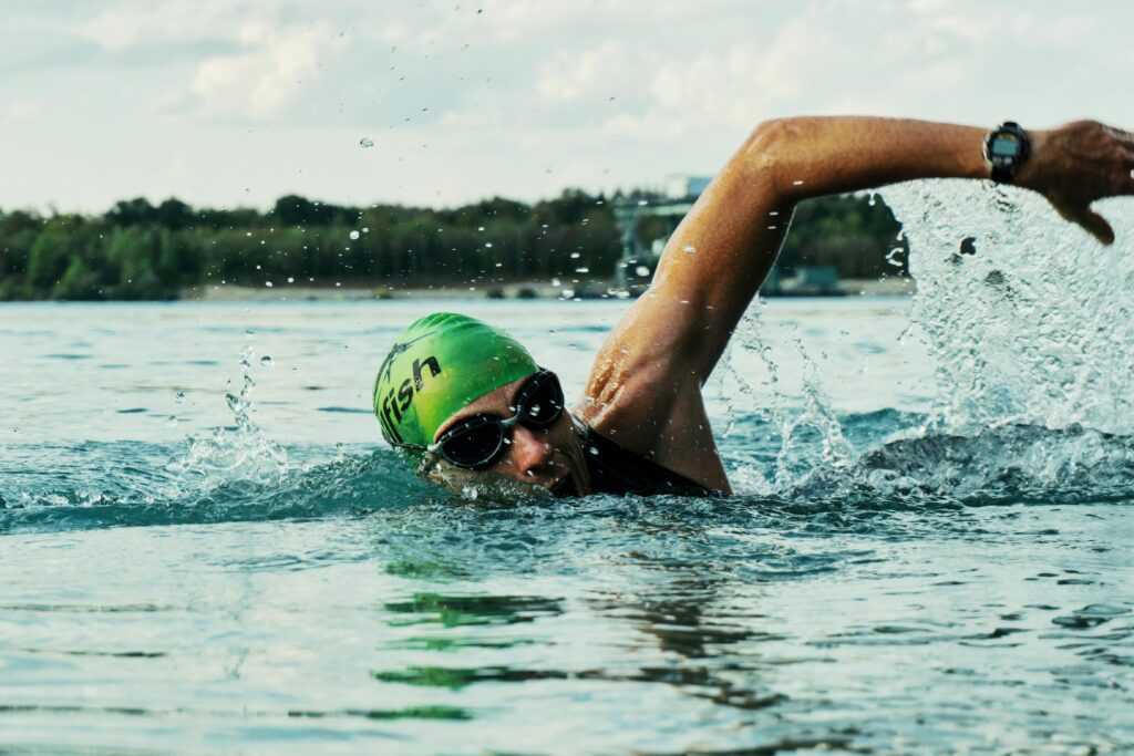 A male swimmer in a green cap and goggles competing in an open water race.