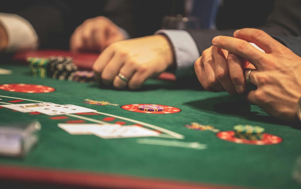 Hands playing blackjack in a casino setting with cards and chips on a green table.